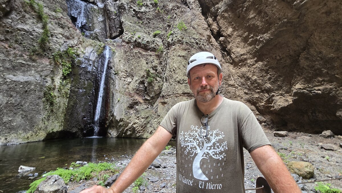 Diabelski Wąwóz na Teneryfie. Marek Dąbrowski pozuje przy wodospadzie Barranco del Infierno, z letnią kaskadą wody w tle.